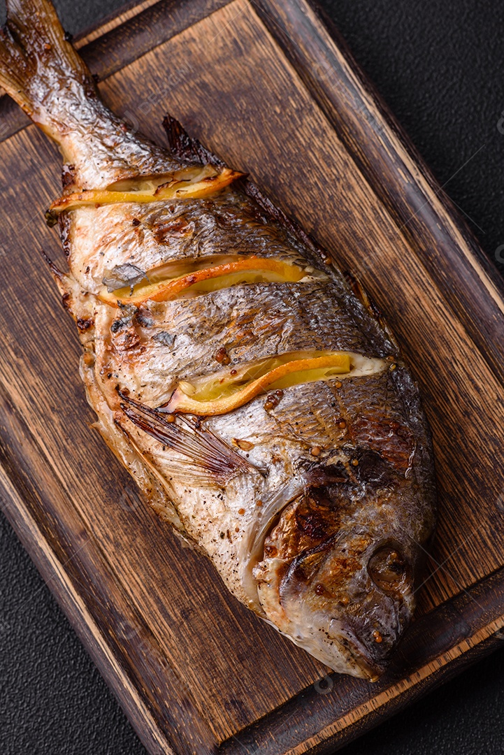 Delicioso dorado assado na grelha com sal, especiarias e ervas sobre um fundo escuro texturizado