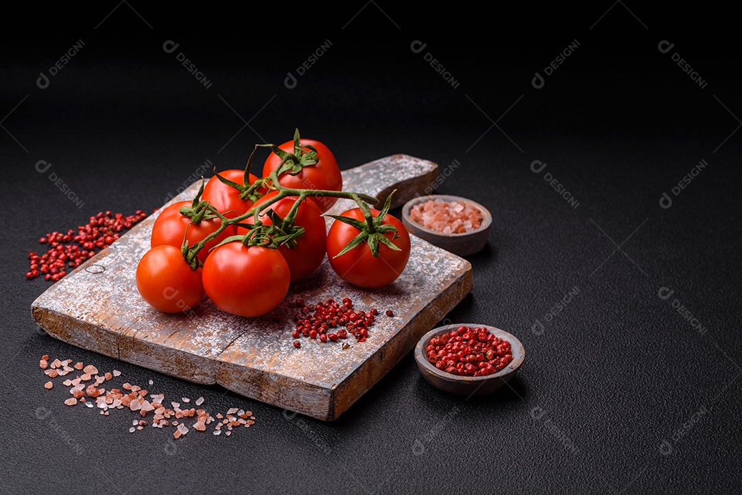 Tomates cereja vermelhos frescos em um galho sobre um fundo escuro de concreto como ingrediente para preparar um prato em casa