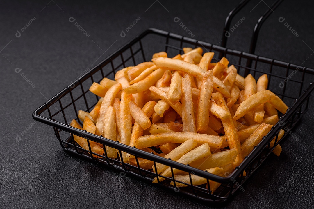 Deliciosas batatas fritas douradas crocantes com sal e especiarias sobre um fundo escuro de concreto