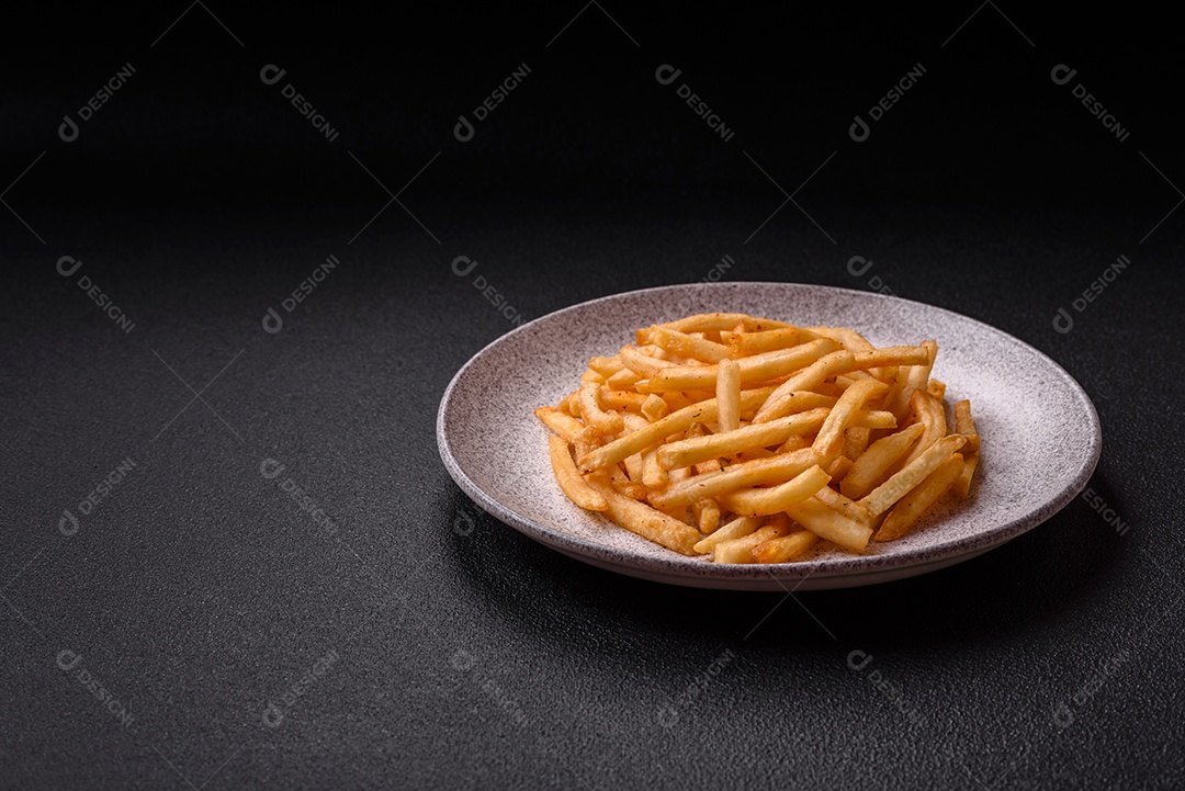 Deliciosas batatas fritas douradas crocantes com sal e especiarias sobre um fundo escuro de concreto