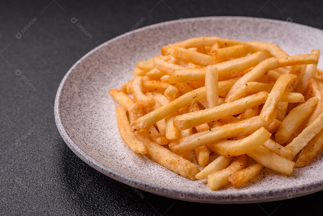 Deliciosas batatas fritas douradas crocantes com sal e especiarias sobre um fundo escuro de concreto