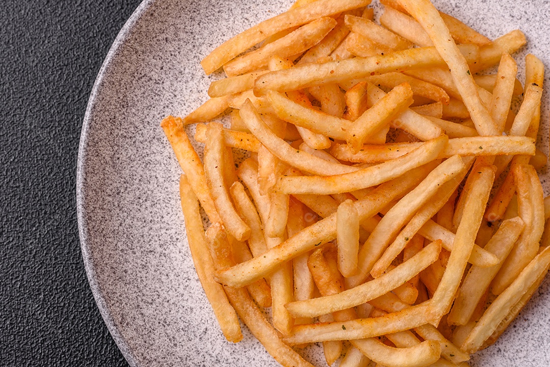 Deliciosas batatas fritas douradas crocantes com sal e especiarias sobre um fundo escuro de concreto