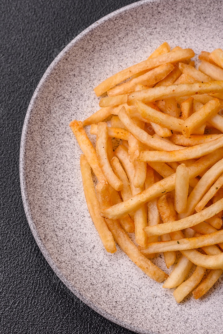 Deliciosas batatas fritas douradas crocantes com sal e especiarias sobre um fundo escuro de concreto