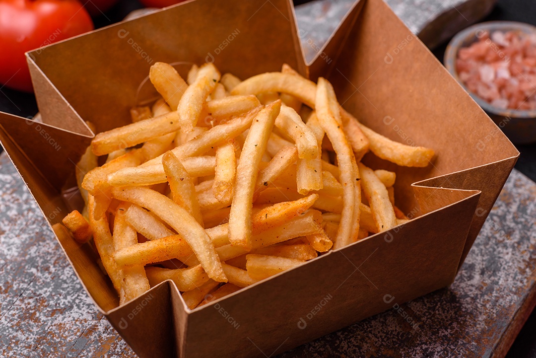 Deliciosas batatas fritas douradas crocantes com sal e especiarias sobre um fundo escuro de concreto