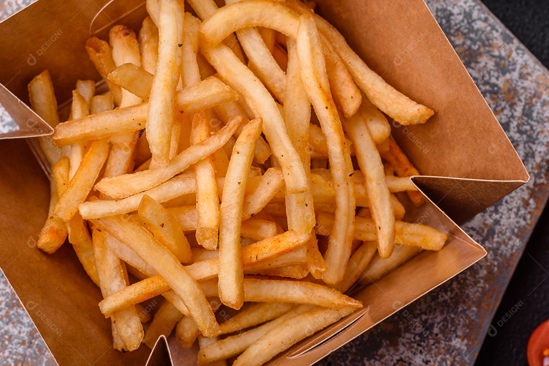 Deliciosas batatas fritas douradas crocantes com sal e especiarias sobre um fundo escuro de concreto