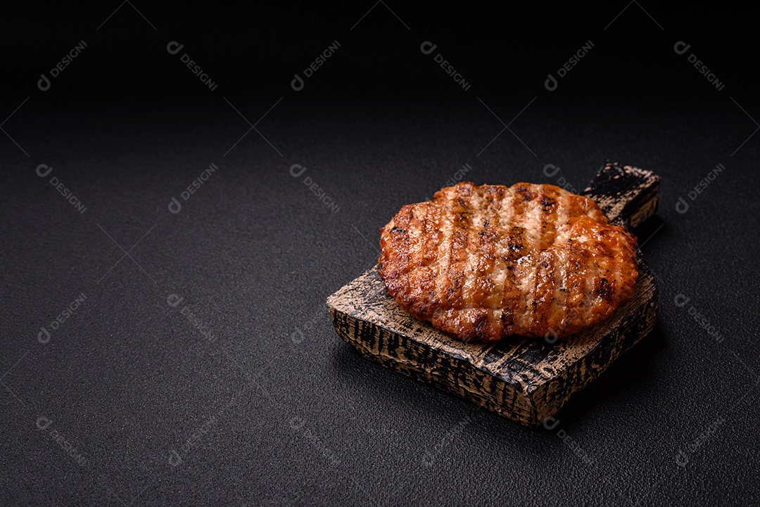 Delicioso filé de frango grelhado fresco com especiarias e ervas em um fundo escuro de concreto. Um prato cozido no fogo