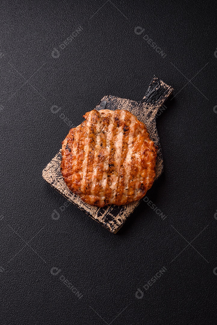 Delicioso filé de frango grelhado fresco com especiarias e ervas em um fundo escuro de concreto. Um prato cozido no fogo