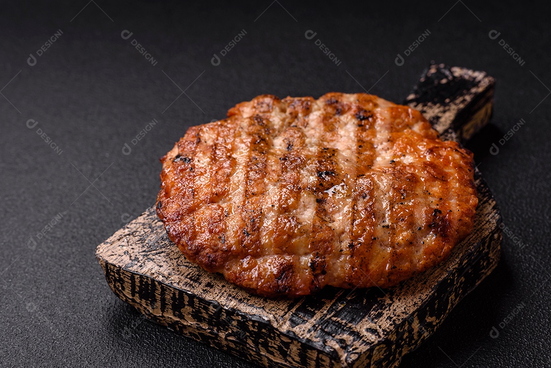 Delicioso filé de frango grelhado fresco com especiarias e ervas em um fundo escuro de concreto. Um prato cozido no fogo