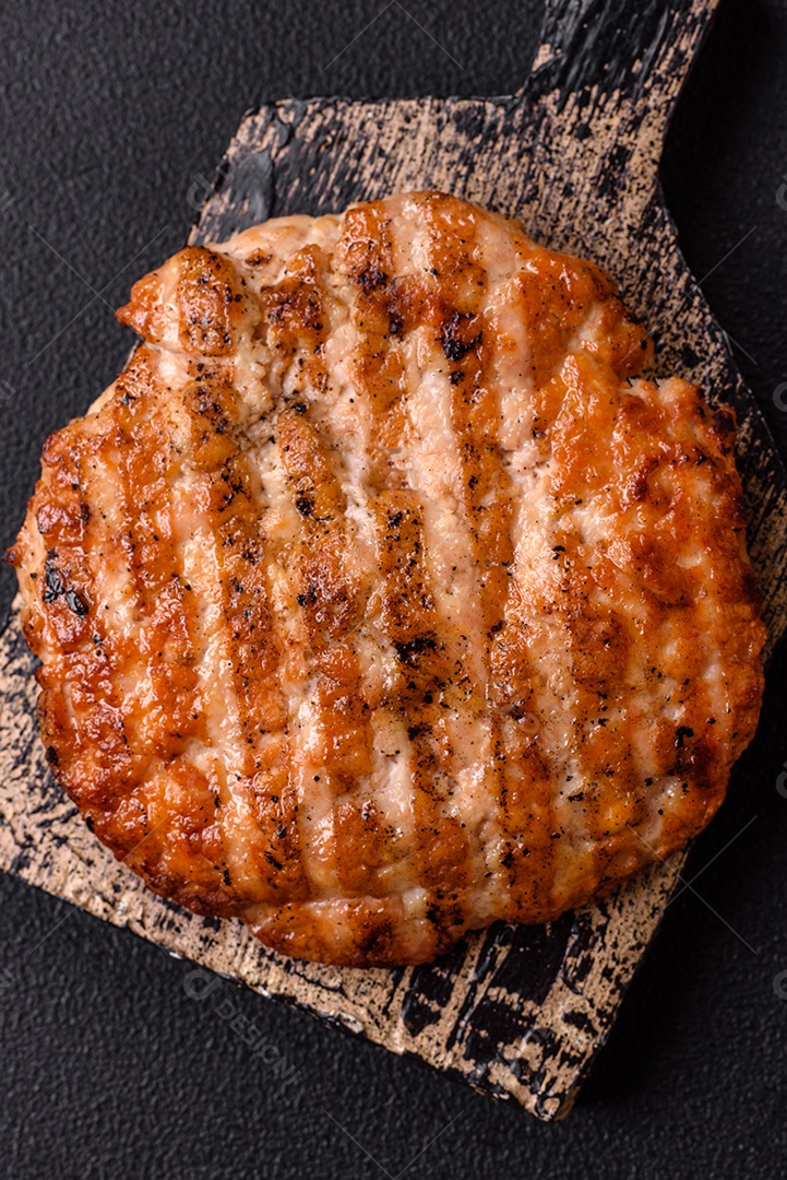 Delicioso filé de frango grelhado fresco com especiarias e ervas em um fundo escuro de concreto. Um prato cozido no fogo