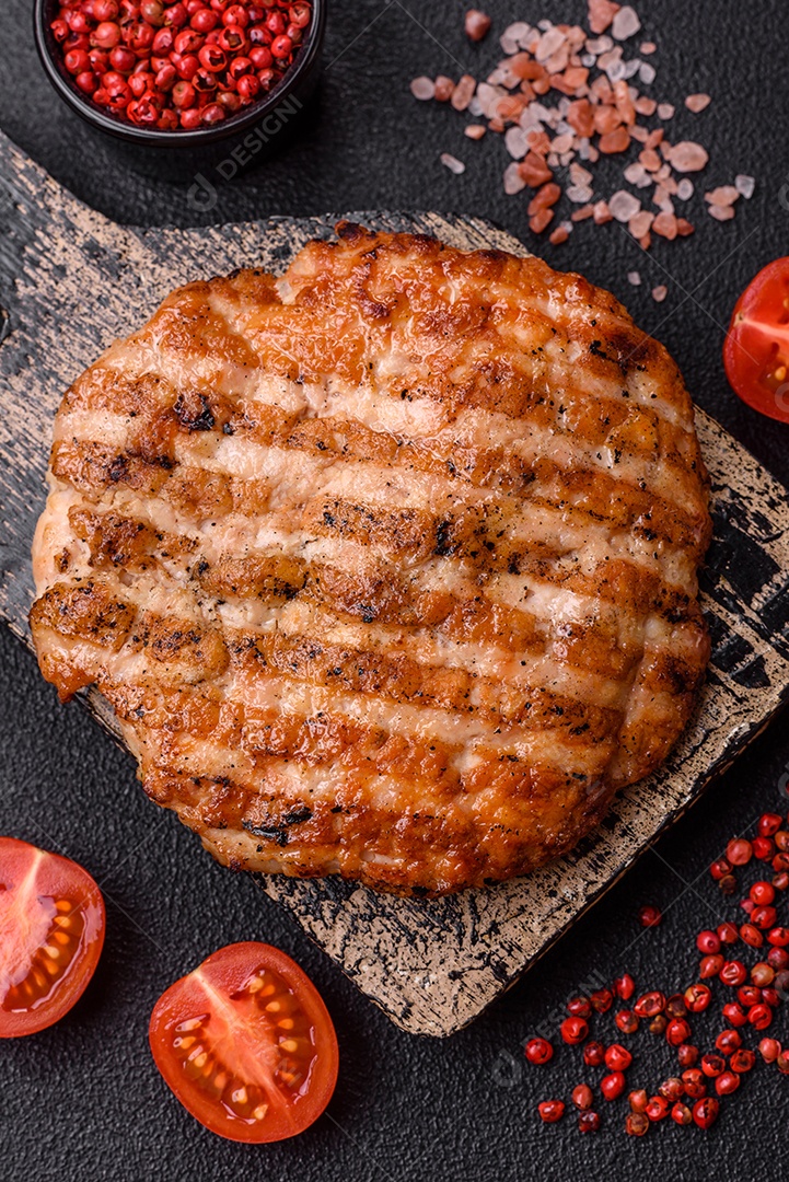 Delicioso filé de frango grelhado fresco com especiarias e ervas em um fundo escuro de concreto. Um prato cozido no fogo