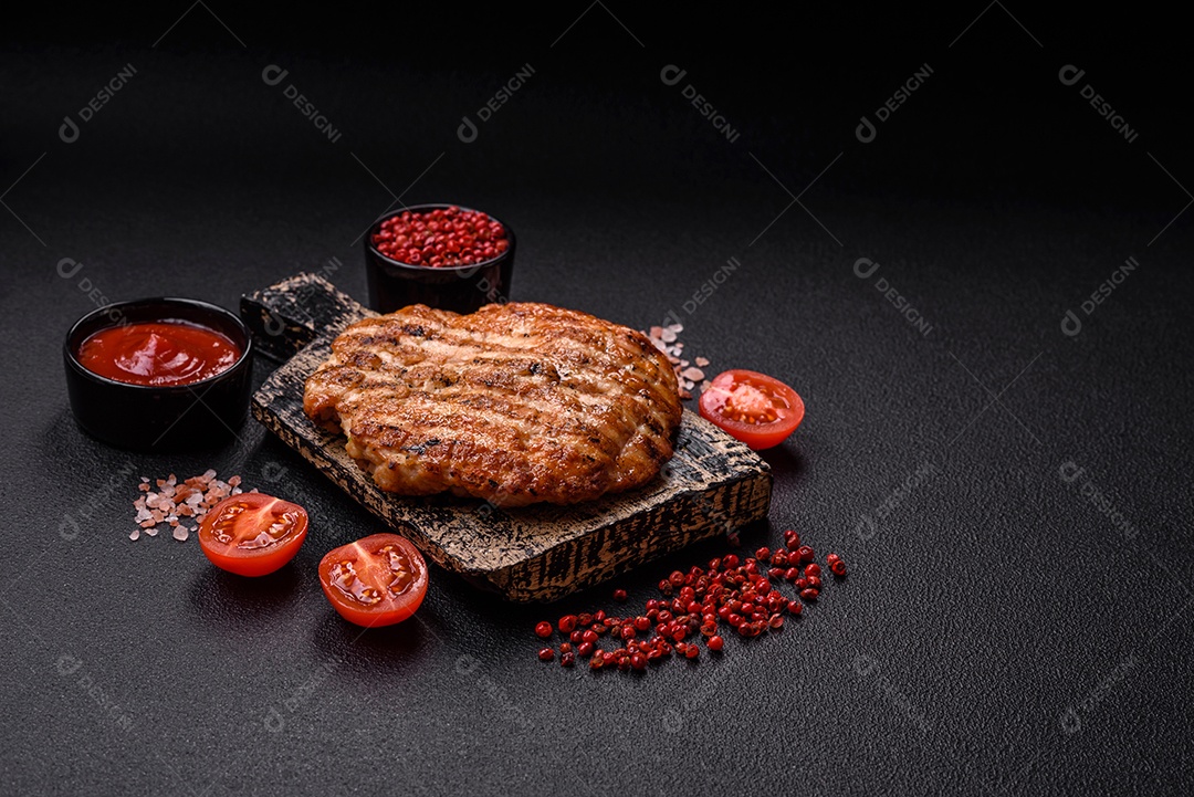 Delicioso filé de frango grelhado fresco com especiarias e ervas em um fundo escuro de concreto. Um prato cozido no fogo