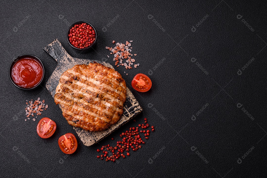 Delicioso filé de frango grelhado fresco com especiarias e ervas em um fundo escuro de concreto. Um prato cozido no fogo