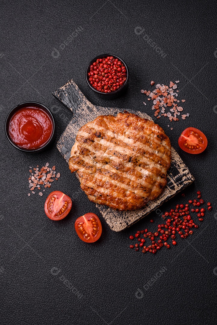 Delicioso filé de frango grelhado fresco com especiarias e ervas em um fundo escuro de concreto. Um prato cozido no fogo