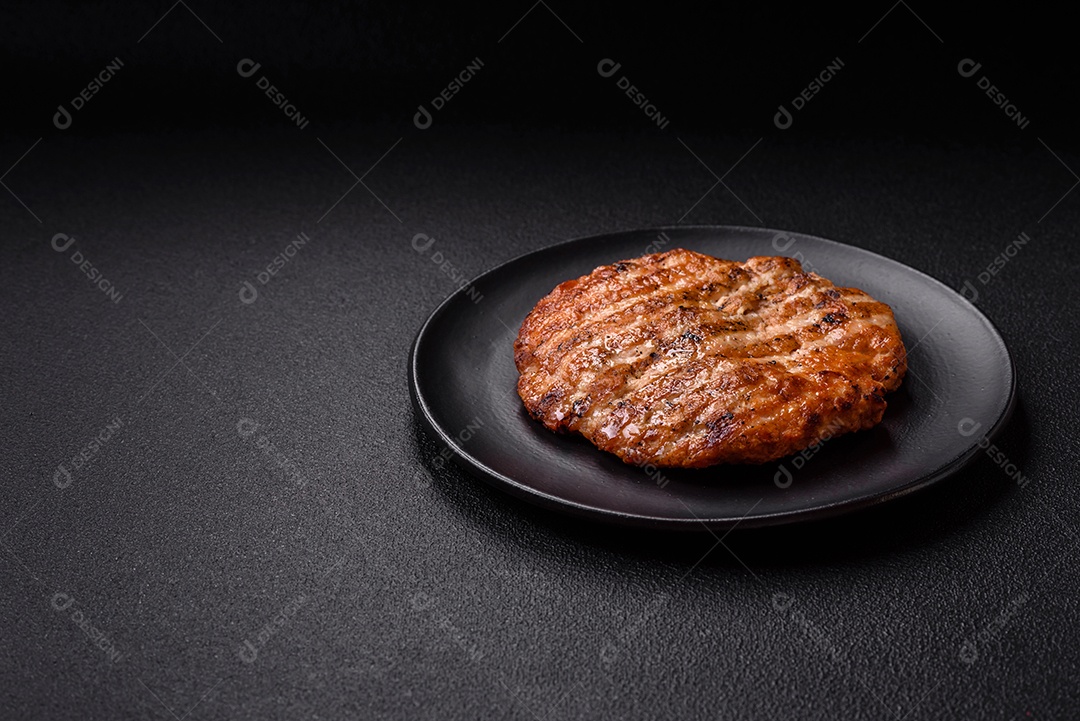 Delicioso filé de frango grelhado fresco com especiarias e ervas em um fundo escuro de concreto. Um prato cozido no fogo