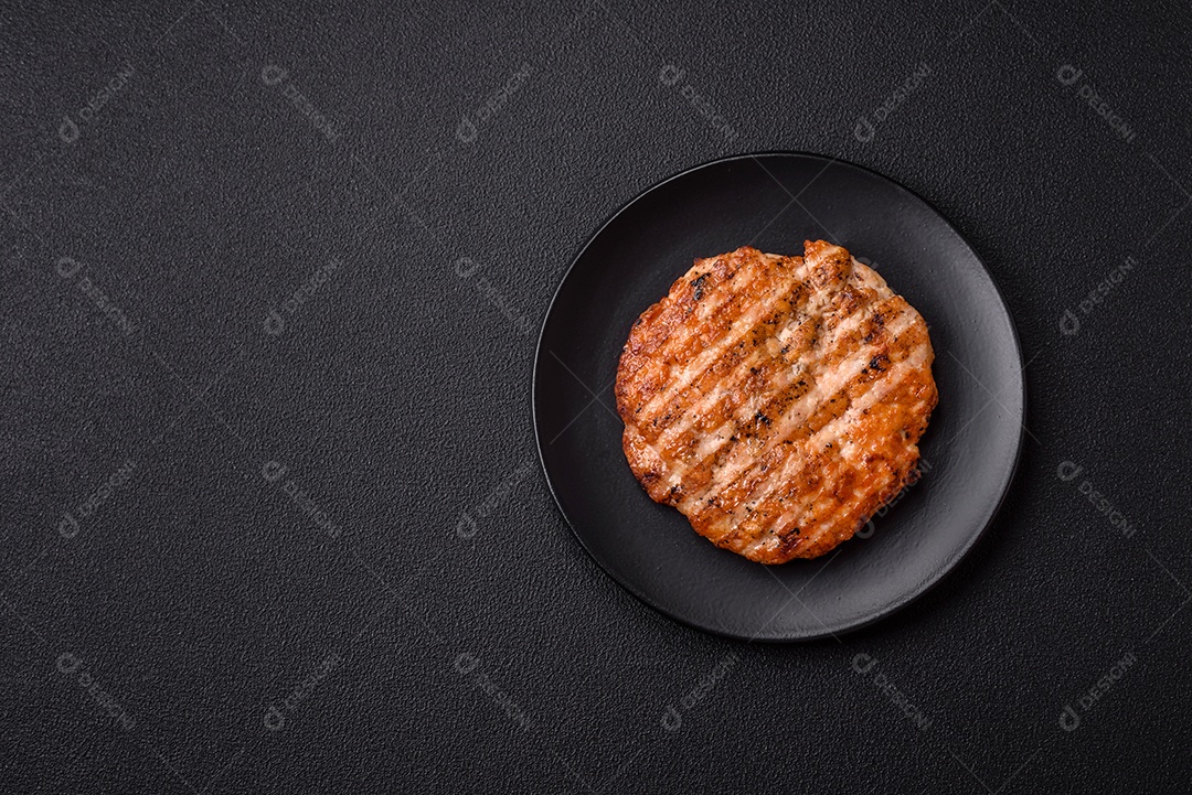 Delicioso filé de frango grelhado fresco com especiarias e ervas em um fundo escuro de concreto. Um prato cozido no fogo