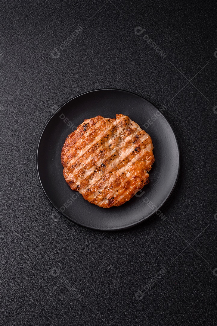 Delicioso filé de frango grelhado fresco com especiarias e ervas em um fundo escuro de concreto. Um prato cozido no fogo