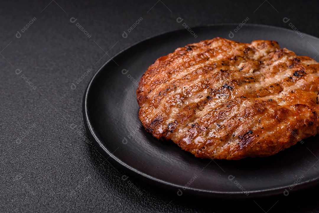 Delicioso filé de frango grelhado fresco com especiarias e ervas em um fundo escuro de concreto. Um prato cozido no fogo