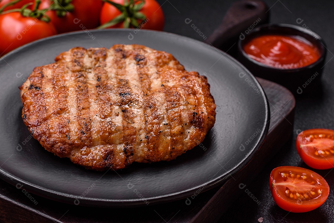 Delicioso filé de frango grelhado fresco com especiarias e ervas em um fundo escuro de concreto. Um prato cozido no fogo