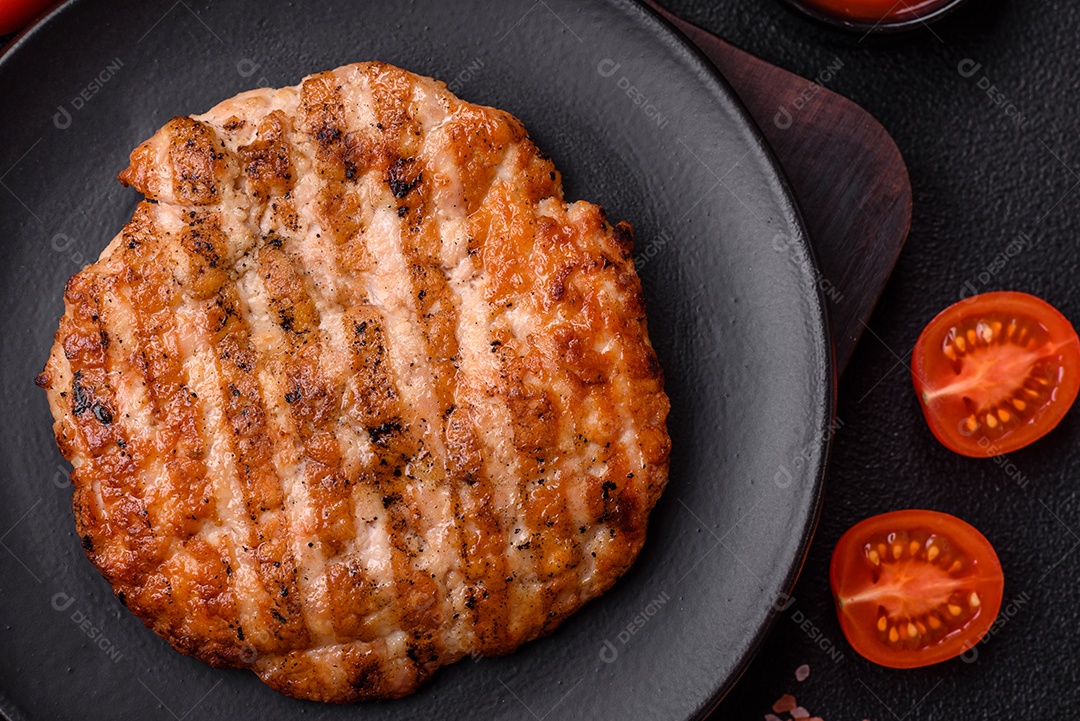 Delicioso filé de frango grelhado fresco com especiarias e ervas em um fundo escuro de concreto. Um prato cozido no fogo