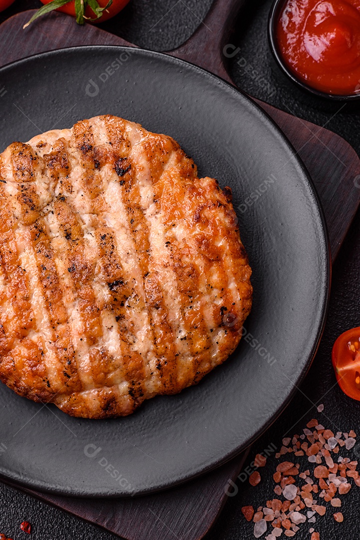 Delicioso filé de frango grelhado fresco com especiarias e ervas em um fundo escuro de concreto. Um prato cozido no fogo