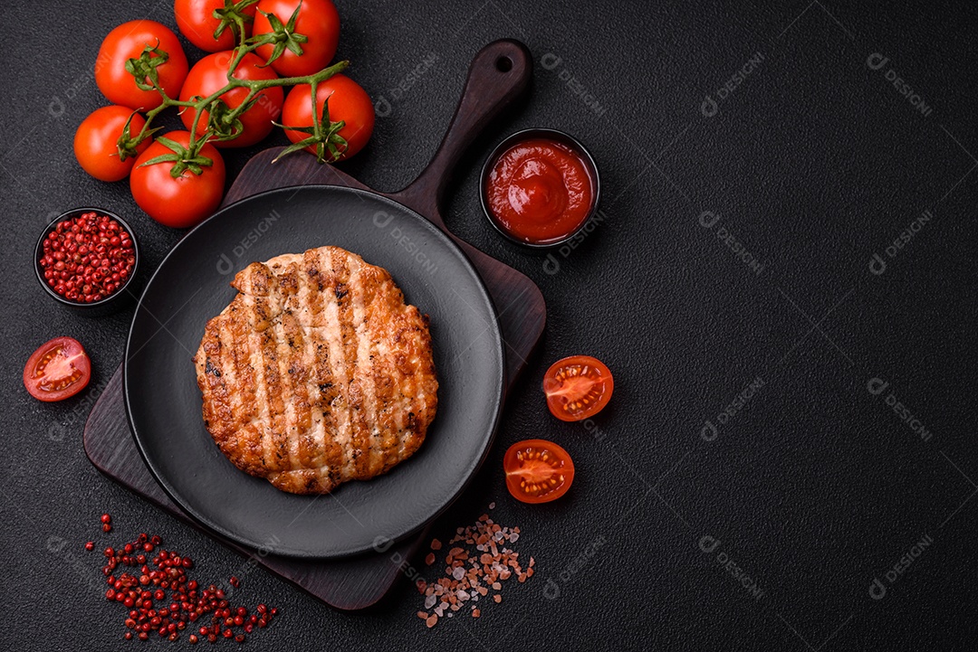 Delicioso filé de frango grelhado fresco com especiarias e ervas em um fundo escuro de concreto. Um prato cozido no fogo