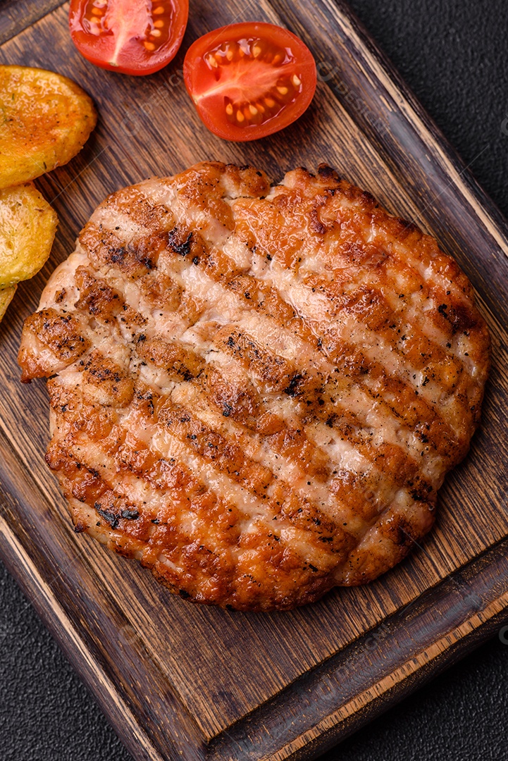 Delicioso filé de frango grelhado fresco com especiarias e ervas em um fundo escuro de concreto. Um prato cozido no fogo