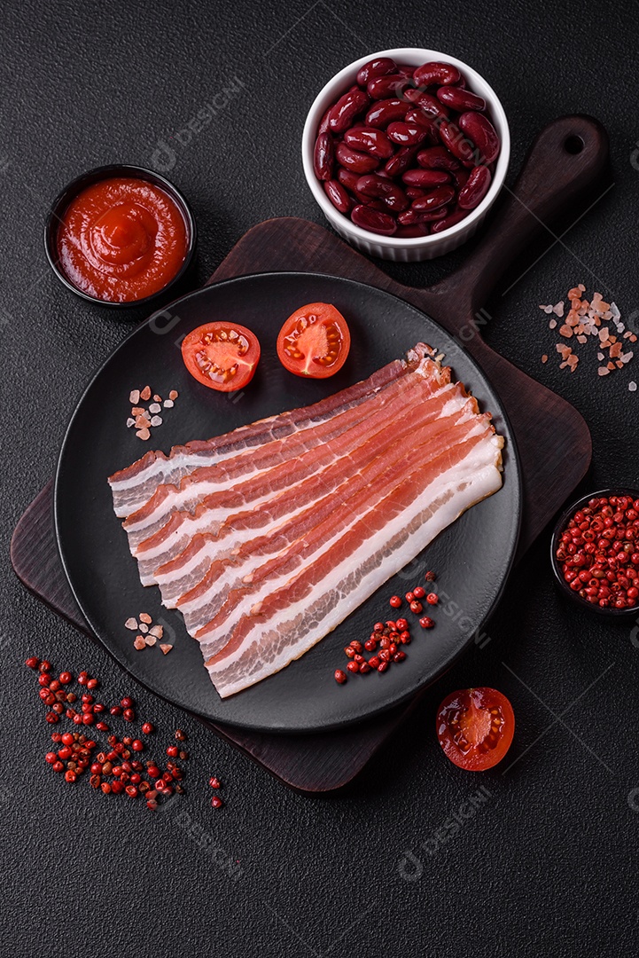 Delicioso bacon frito fresco com sal e especiarias sobre fundo escuro como ingrediente para preparar um farto café da manhã