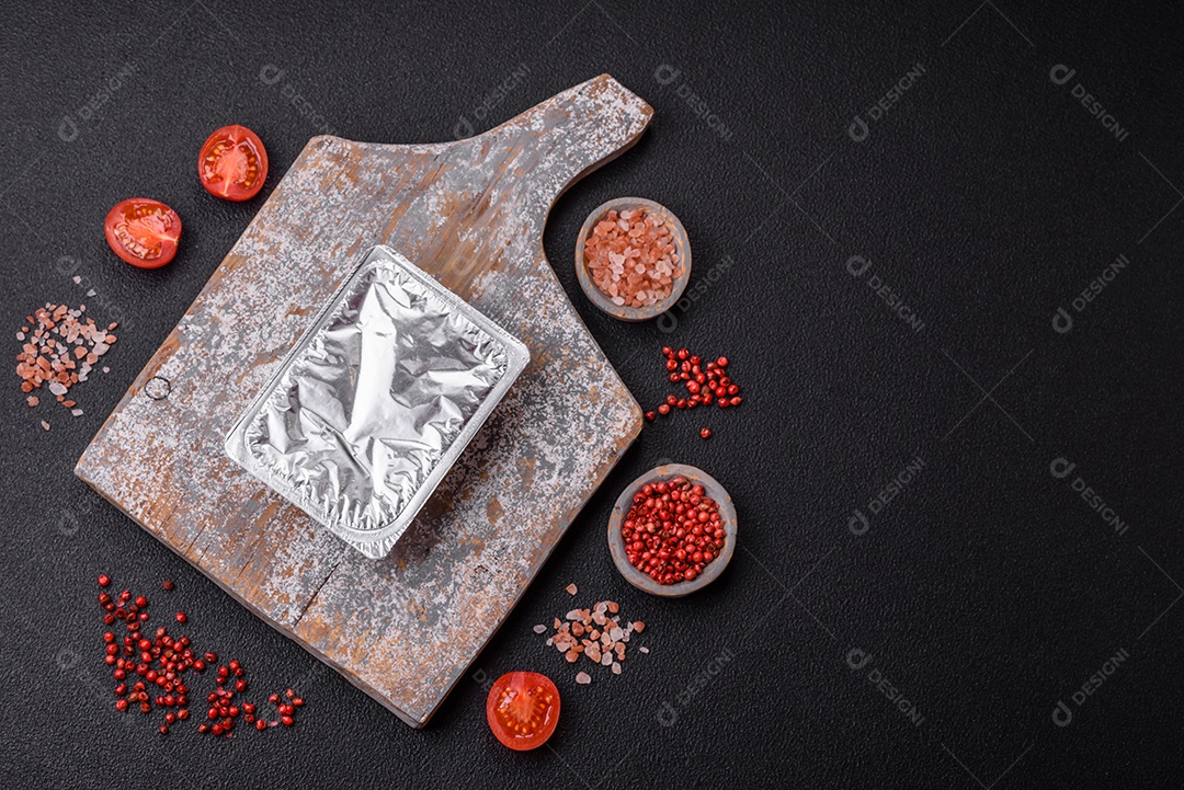 Caixa plástica retangular com iogurte ou queijo hermeticamente selada com tampa de alumínio sobre fundo escuro de concreto