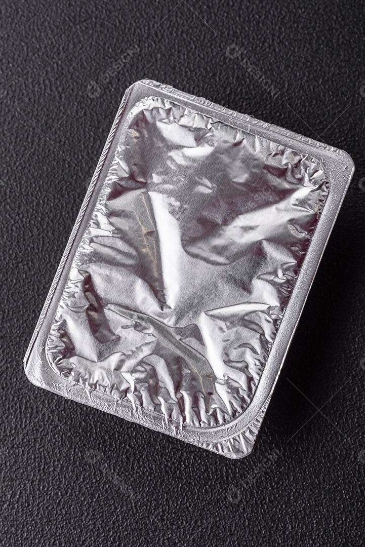 Caixa plástica retangular com iogurte ou queijo hermeticamente selada com tampa de alumínio sobre fundo escuro de concreto