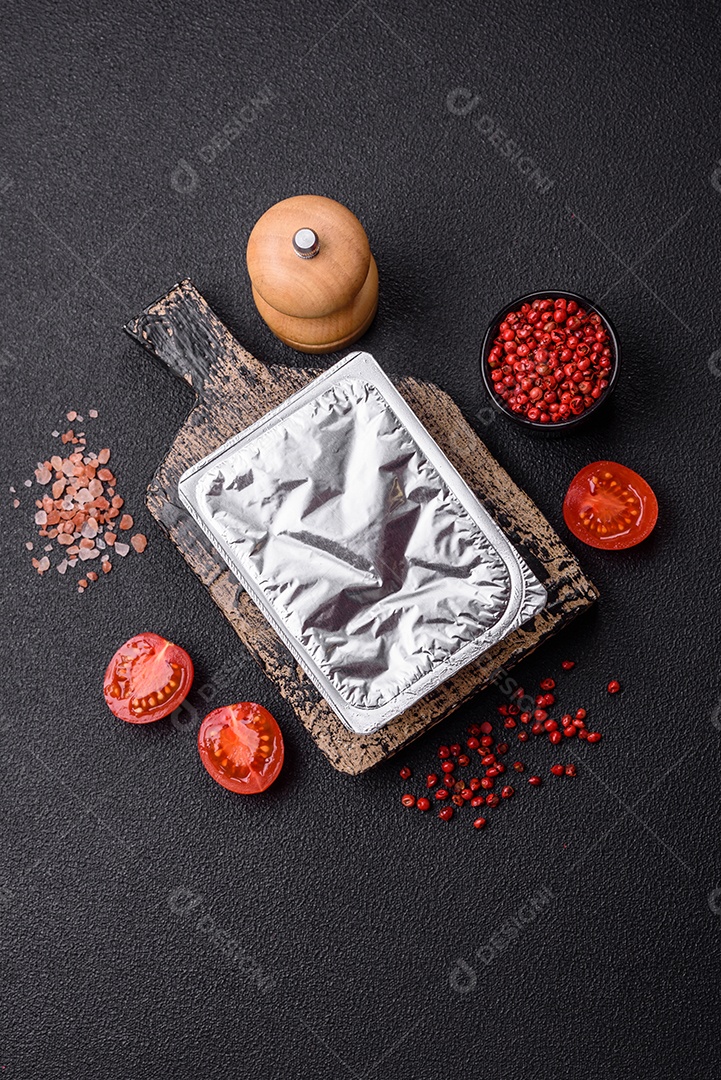 Caixa plástica retangular com iogurte ou queijo hermeticamente selada com tampa de alumínio sobre fundo escuro de concreto