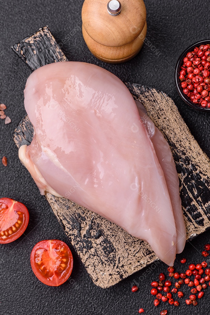 Filé de frango fresco sobre uma mesa de concreto escuro com especiarias e ervas. Preparação para cozinhar pratos de carne
