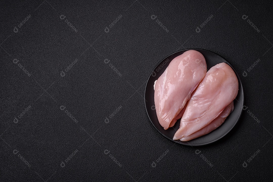 Filé de frango fresco sobre uma mesa de concreto escuro com especiarias e ervas. Preparação para cozinhar pratos de carne