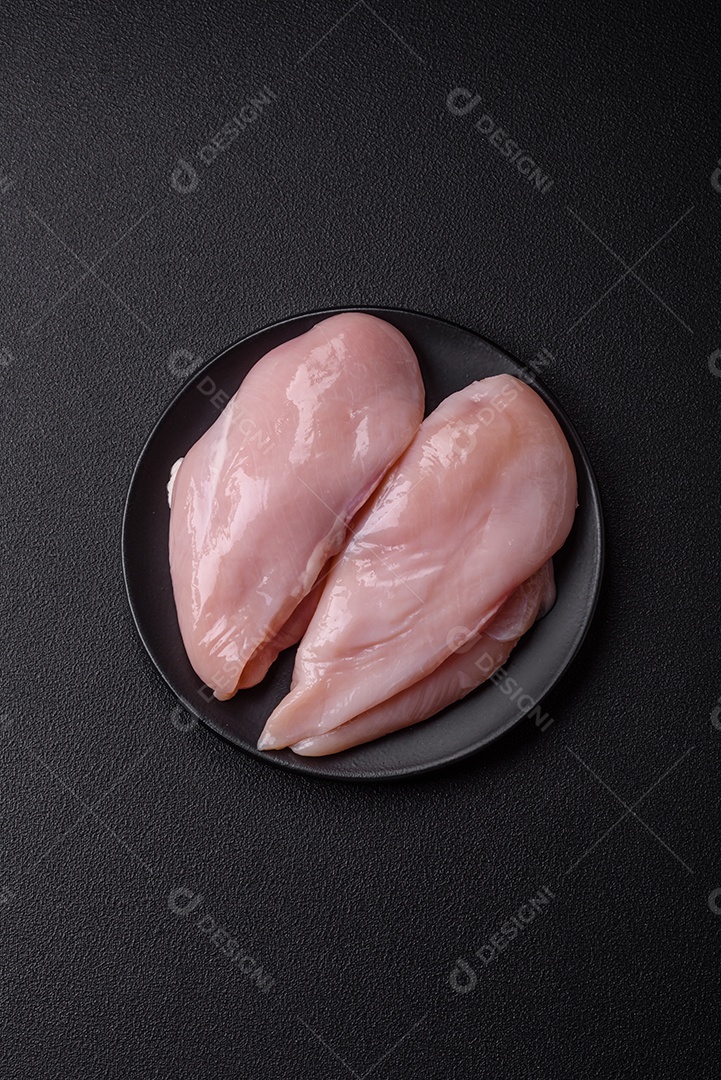 Filé de frango fresco sobre uma mesa de concreto escuro com especiarias e ervas. Preparação para cozinhar pratos de carne