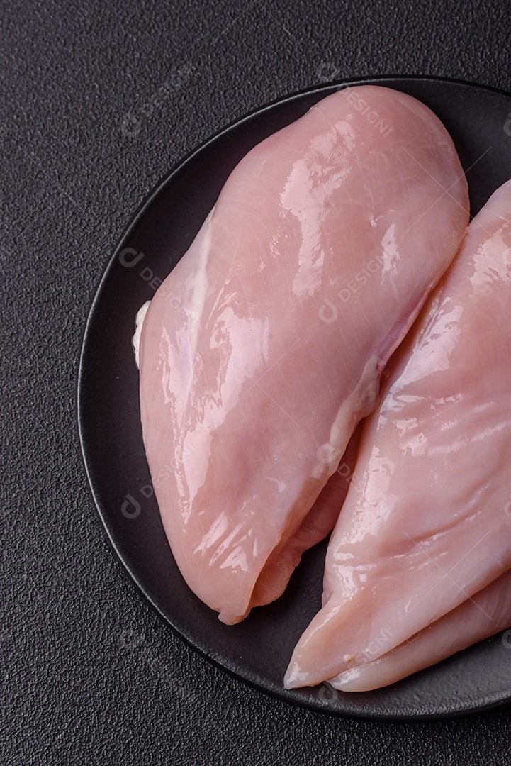 Filé de frango fresco sobre uma mesa de concreto escuro com especiarias e ervas. Preparação para cozinhar pratos de carne