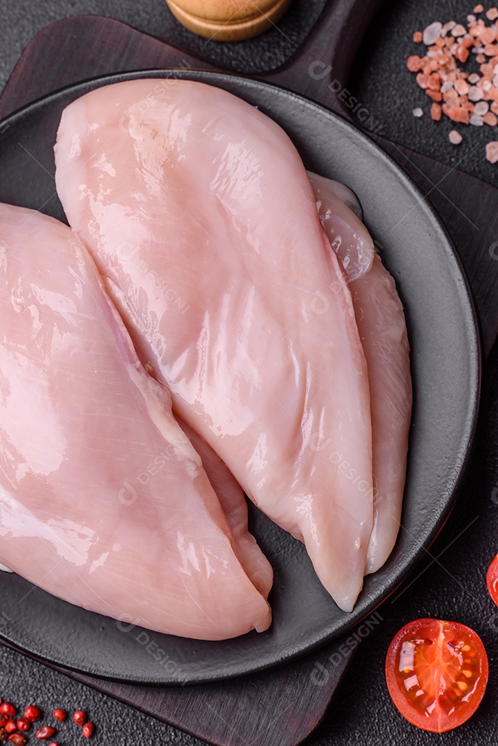 Filé de frango fresco sobre uma mesa de concreto escuro com especiarias e ervas. Preparação para cozinhar pratos de carne