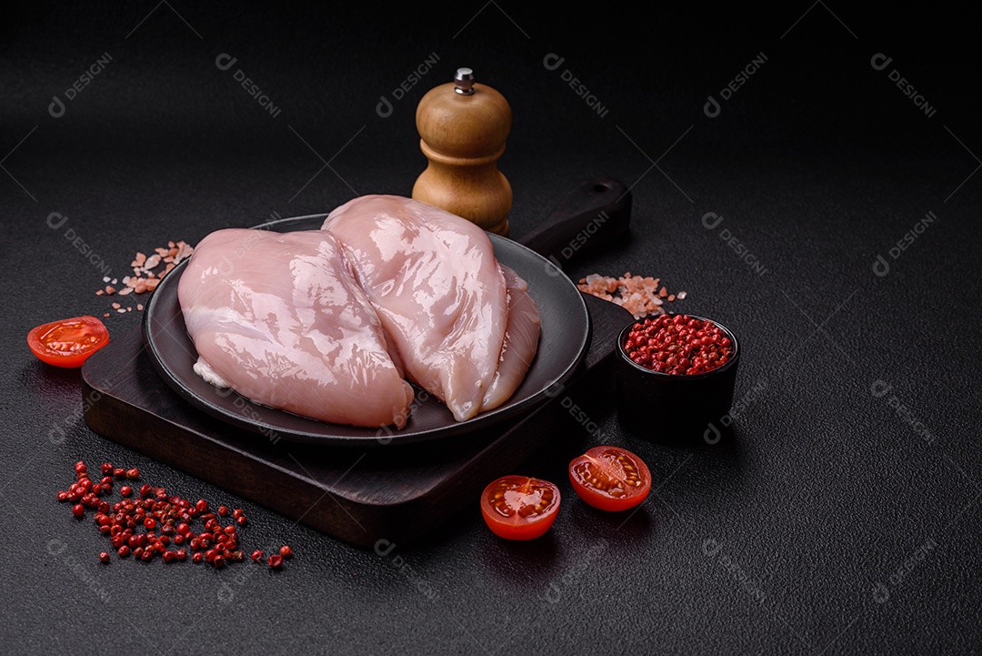 Filé de frango fresco sobre uma mesa de concreto escuro com especiarias e ervas. Preparação para cozinhar pratos de carne