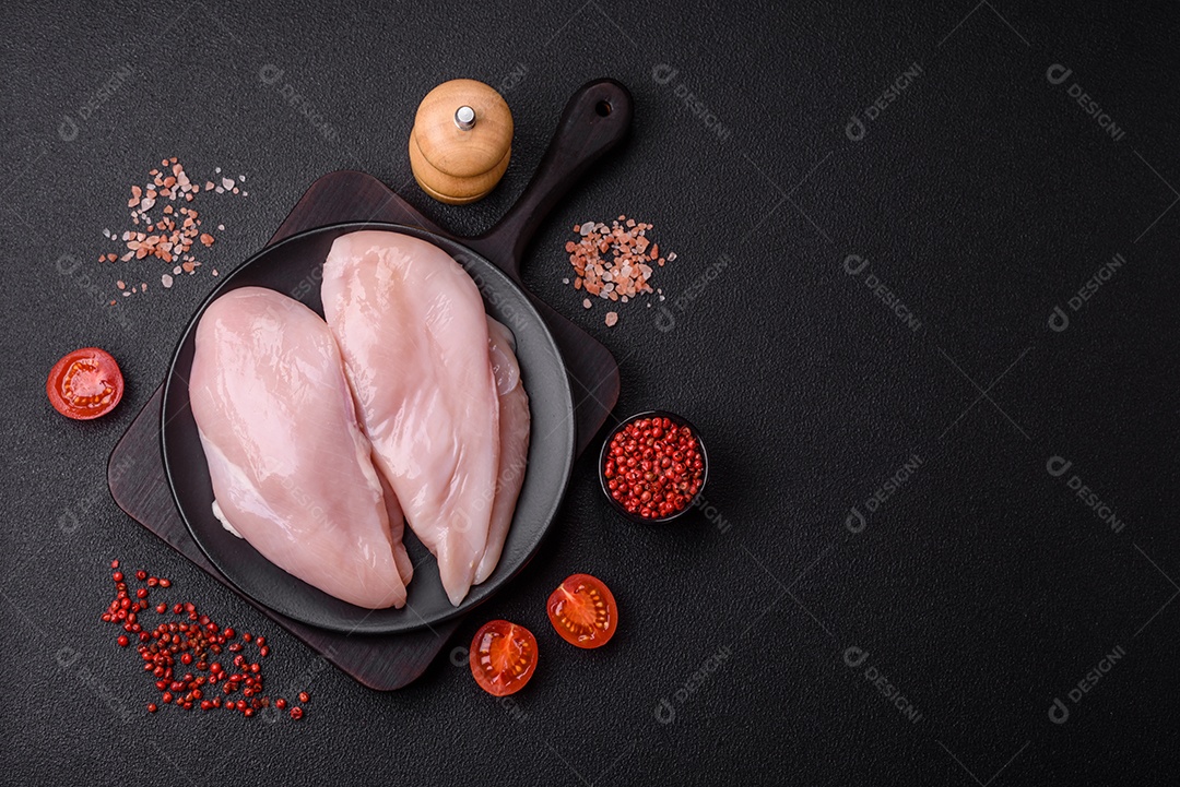 Filé de frango fresco sobre uma mesa de concreto escuro com especiarias e ervas. Preparação para cozinhar pratos de carne