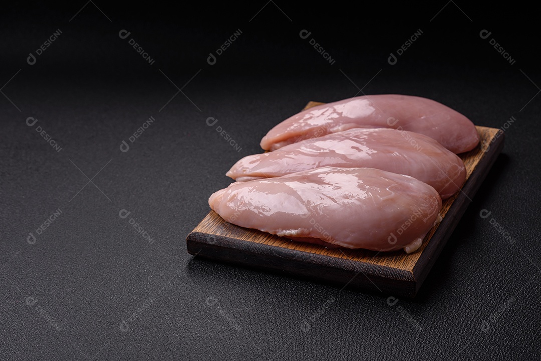 Filé de frango fresco sobre uma mesa de concreto escuro com especiarias e ervas. Preparação para cozinhar pratos de carne