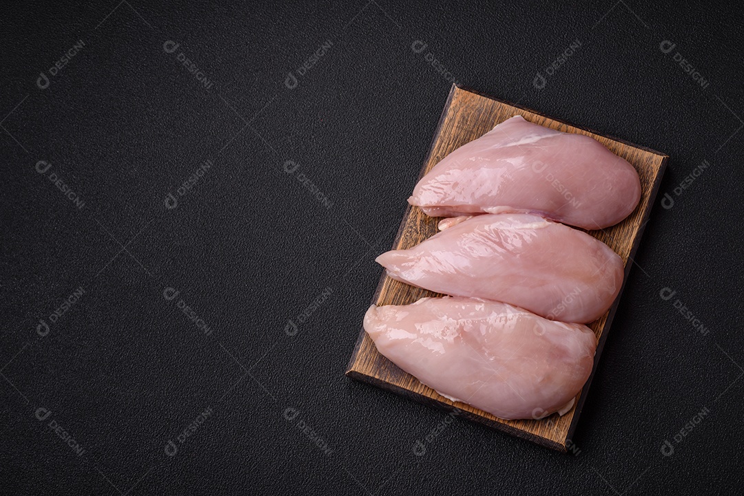 Filé de frango fresco sobre uma mesa de concreto escuro com especiarias e ervas. Preparação para cozinhar pratos de carne