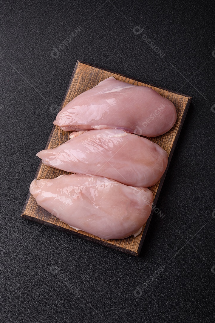 Filé de frango fresco sobre uma mesa de concreto escuro com especiarias e ervas. Preparação para cozinhar pratos de carne