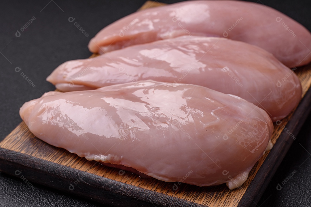 Filé de frango fresco sobre uma mesa de concreto escuro com especiarias e ervas. Preparação para cozinhar pratos de carne