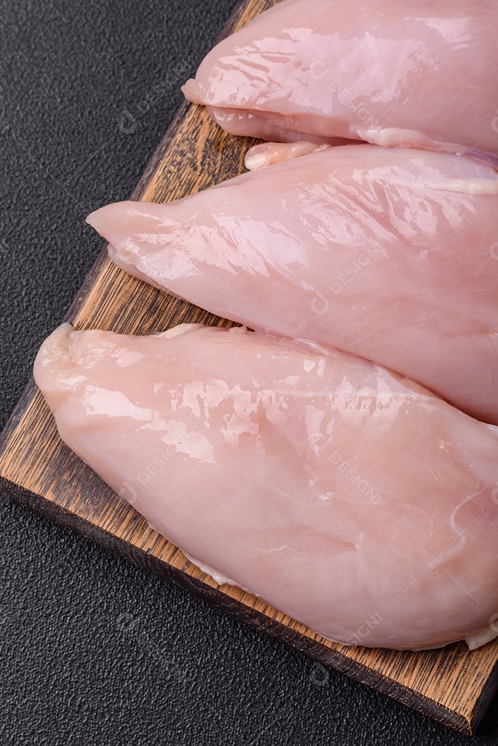 Filé de frango fresco sobre uma mesa de concreto escuro com especiarias e ervas. Preparação para cozinhar pratos de carne