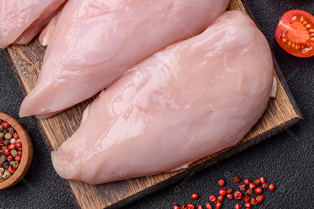 Filé de frango fresco sobre uma mesa de concreto escuro com especiarias e ervas. Preparação para cozinhar pratos de carne