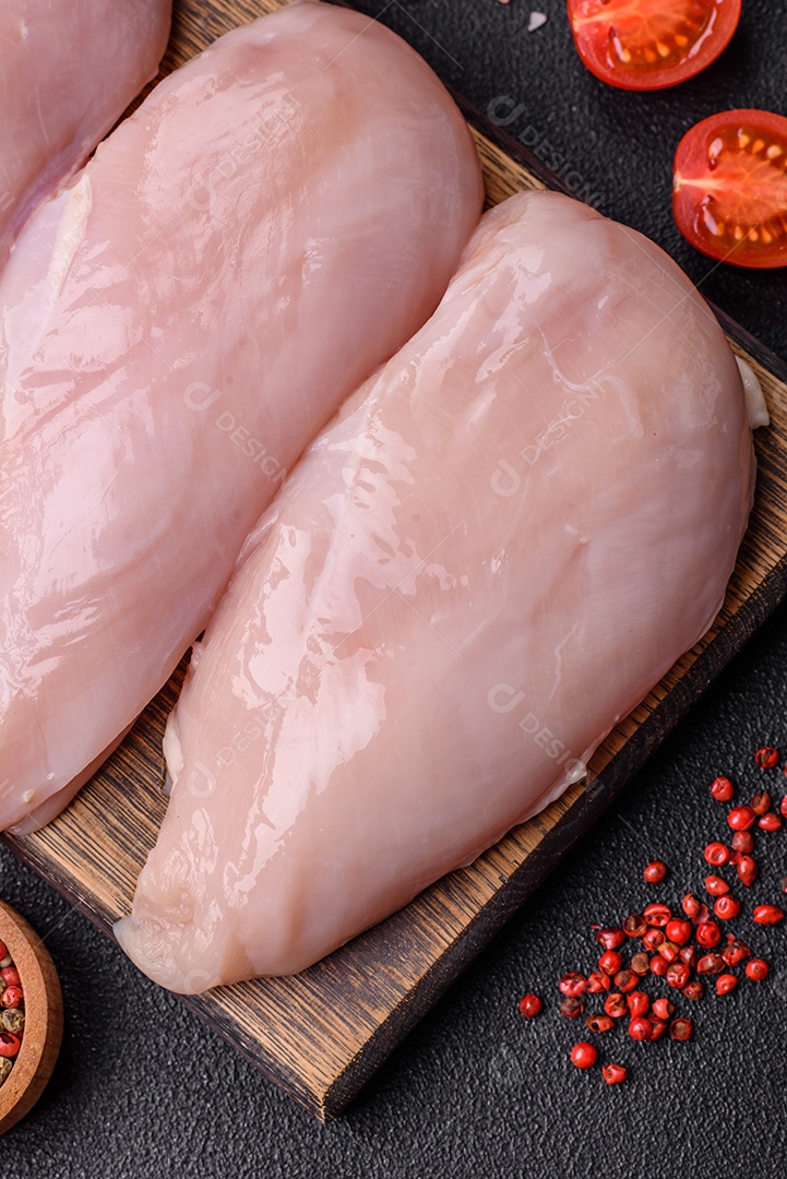 Filé de frango fresco sobre uma mesa de concreto escuro com especiarias e ervas. Preparação para cozinhar pratos de carne