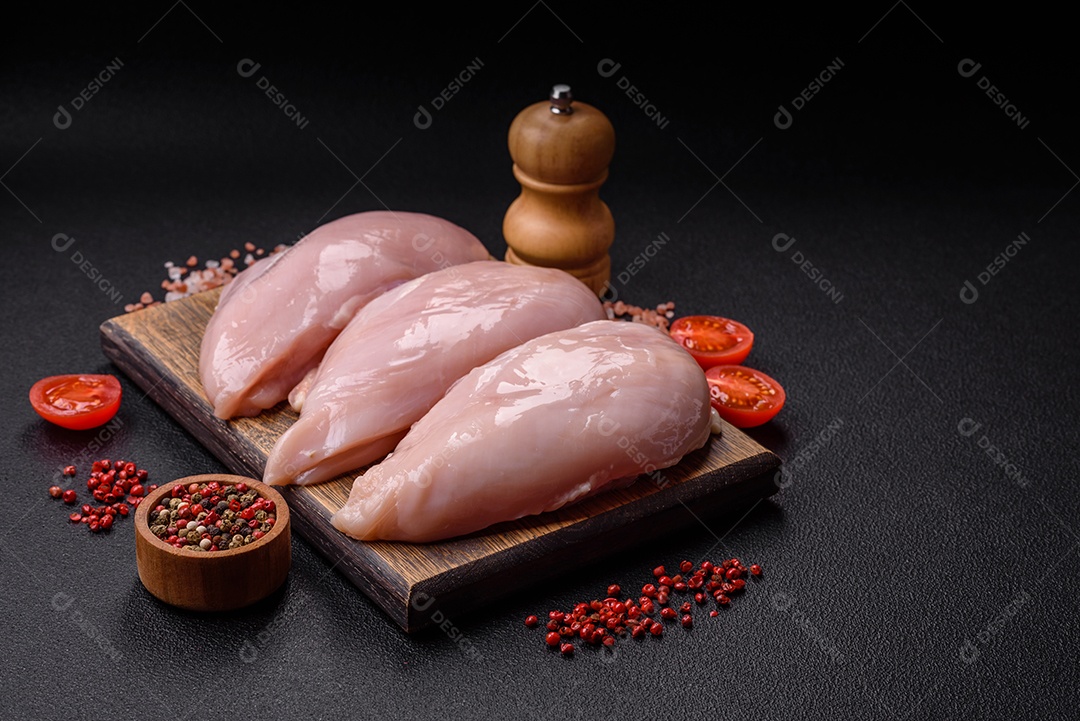 Filé de frango fresco sobre uma mesa de concreto escuro com especiarias e ervas. Preparação para cozinhar pratos de carne