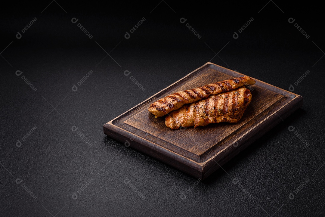 Delicioso filé de frango grelhado fresco com especiarias e ervas em um fundo escuro de concreto. Um prato cozido no fogo