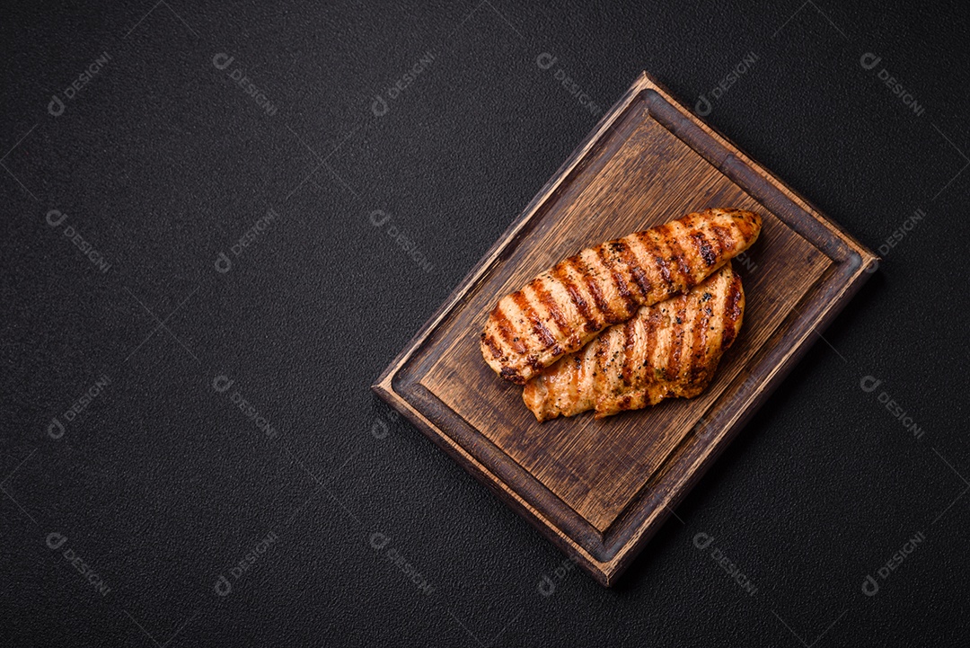 Delicioso filé de frango grelhado fresco com especiarias e ervas em um fundo escuro de concreto. Um prato cozido no fogo