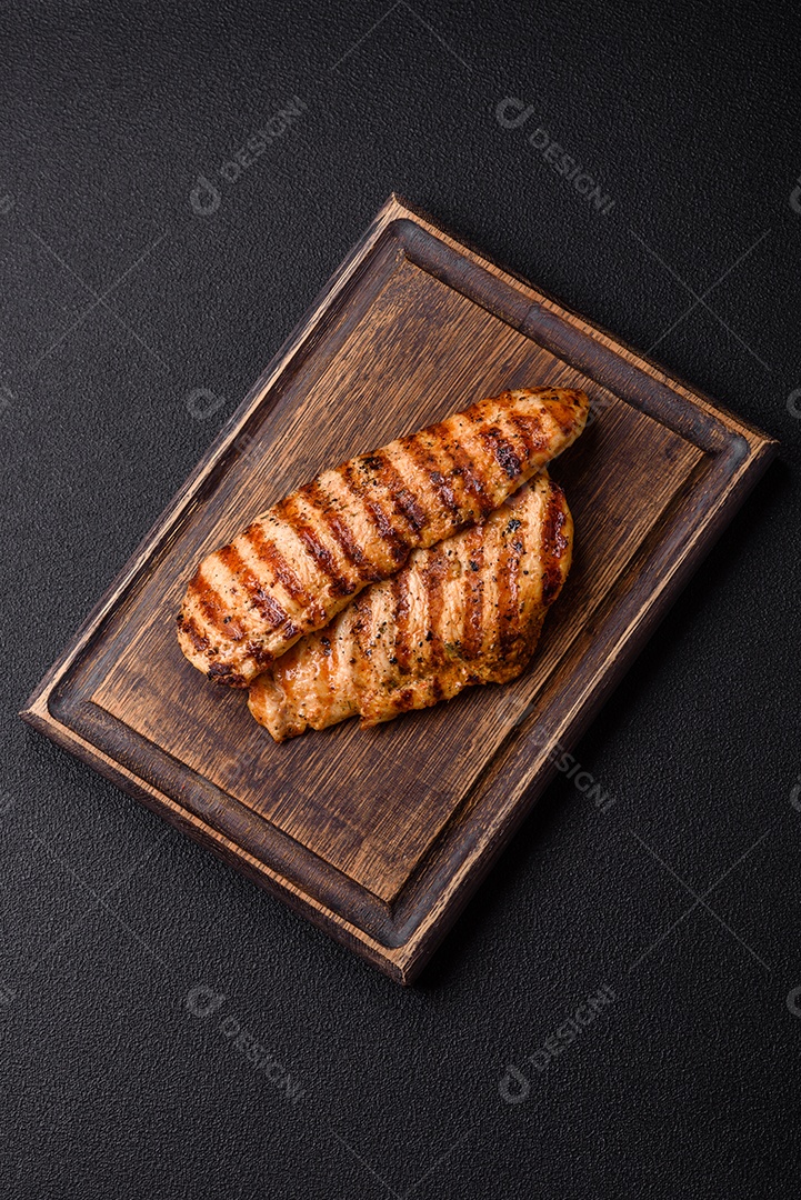 Delicioso filé de frango grelhado fresco com especiarias e ervas em um fundo escuro de concreto. Um prato cozido no fogo