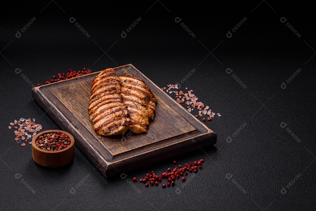 Delicioso filé de frango grelhado fresco com especiarias e ervas em um fundo escuro de concreto. Um prato cozido no fogo