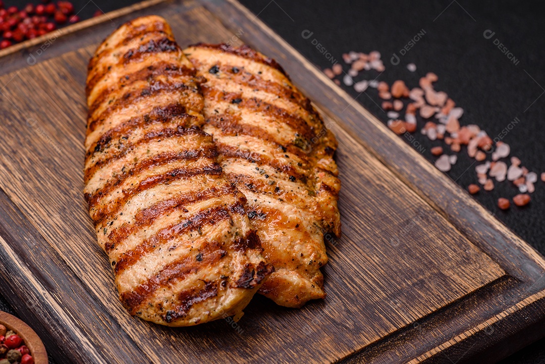 Delicioso filé de frango grelhado fresco com especiarias e ervas em um fundo escuro de concreto. Um prato cozido no fogo